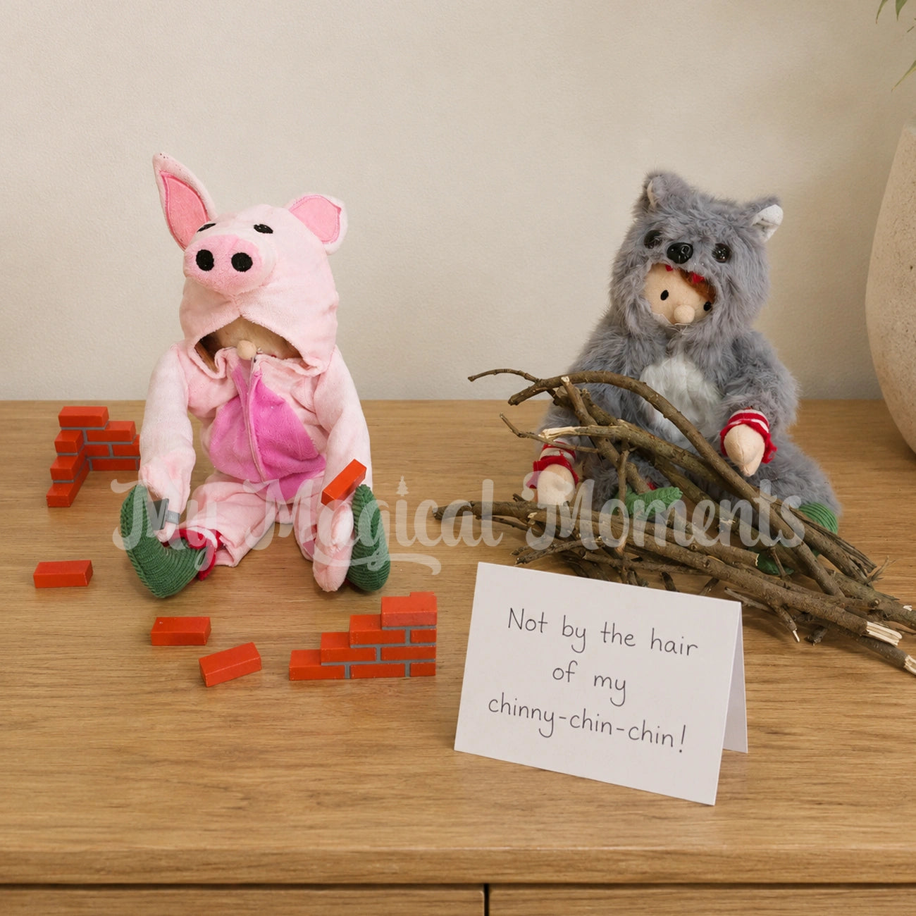 Elf wearing a pig costume building a brick home, a second elf is wearing a wolf costume with sticks, there is a note that says not by the hair of my chinny-chin-chin