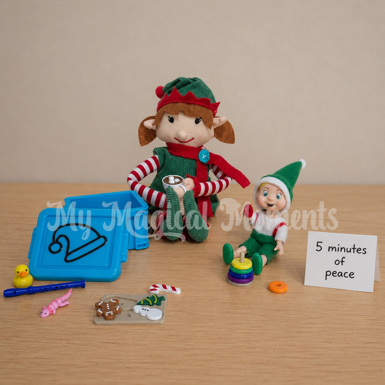 An elf For Christmas holding a hot cocoa, with a toddler elf playing with ring stacker toy, there is a blue mini elf storage container, a small rubber duck, a tiny recorder, a pink axolotl fidget and a puzzle board. There is a hand written note that say 5 minutes of peace