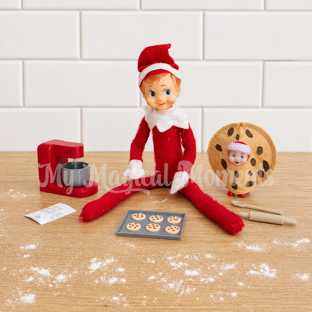 Elf With mini tray of Chocolate chip cookies and baking set. There is a baby elf dressed in a mini cookie outfit and a cookie recipe