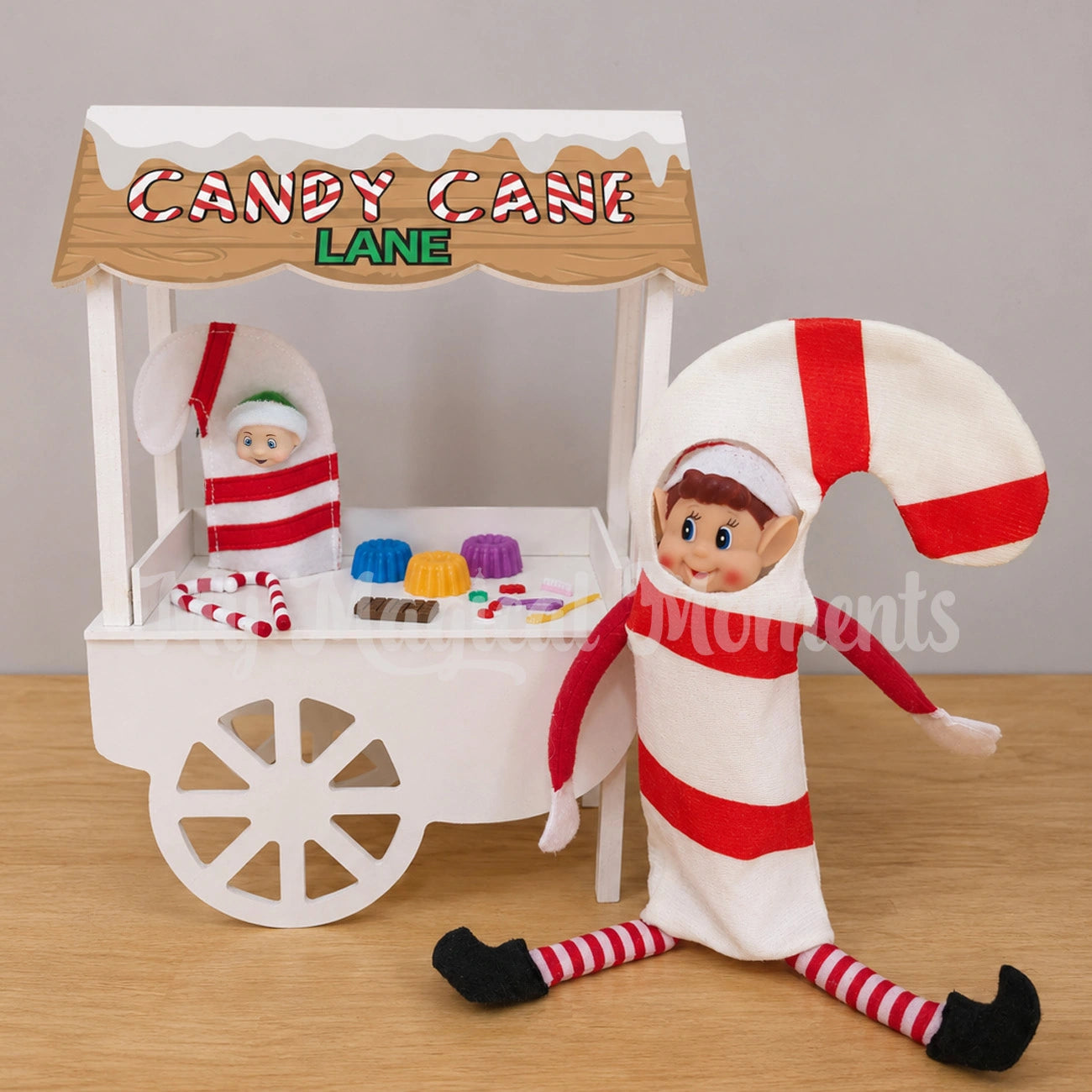 Elf dressed as a candy cane, a baby wearing a candy cane costume, on a candy stand selling candy canes, jelly, chocolate, and lollies