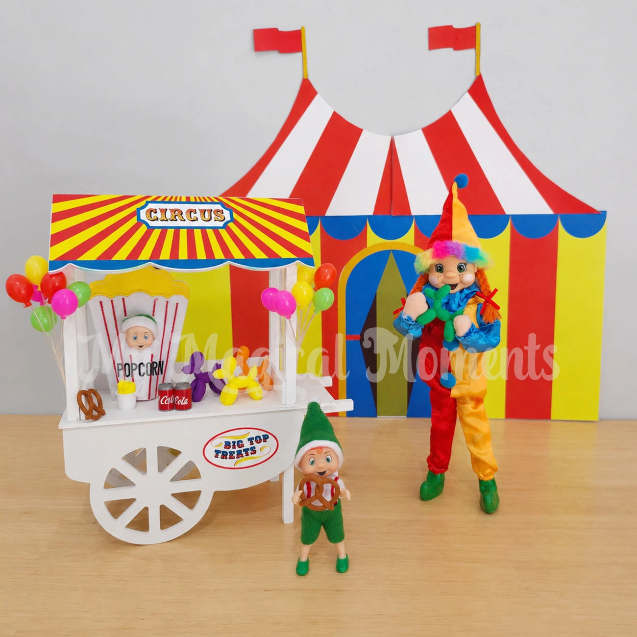 Orange hair elf wearing a clown costume, in front of a printable circus tent, a cart selling mini toy poodle balloons, miniature cola cans, fries and pretzels. There is a baby elf dressed as a popcorn and balloons. The toddler elf is eating a pretzel