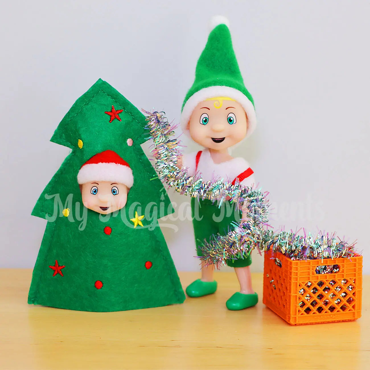 Elf baby wearing a tree costume being decorated by a blonde hair elf toddler