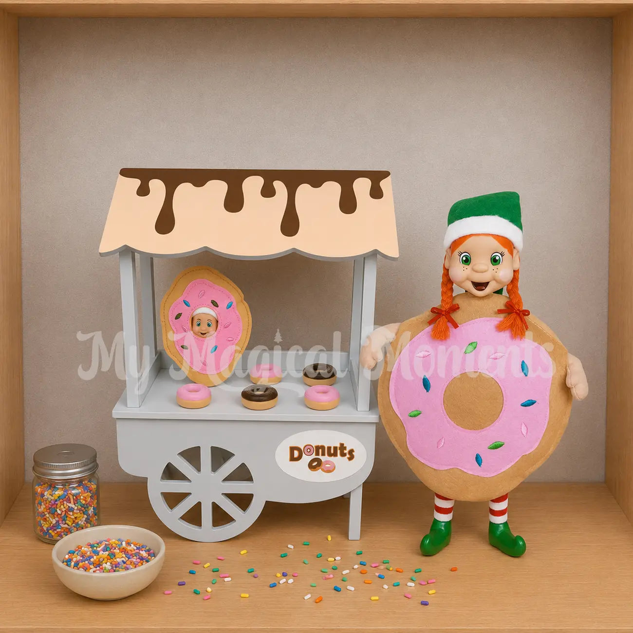 Elf dressed as a donut standing in front of a doughnut store with a baby elf dressed as a donut