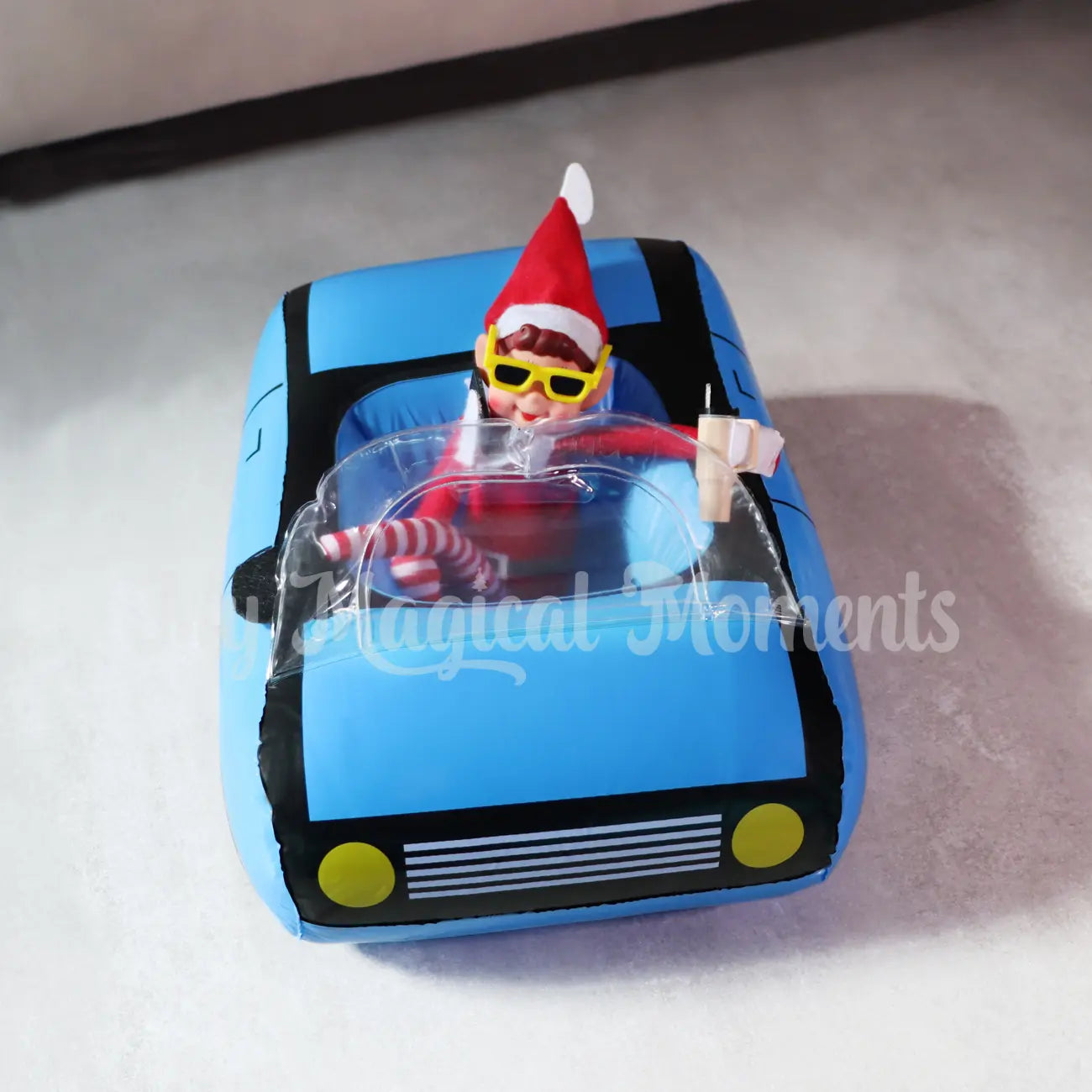 ELves behavin badly talking on a mini elf phone drinking a stanley cup in a mini car with sunglasses