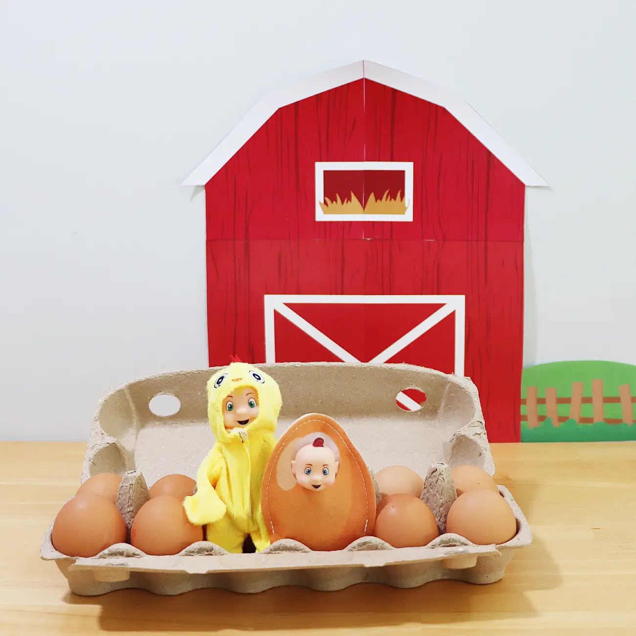 Toddler Elf wearing a chick costume with an elf baby wearing an egg costume in an egg carton in front of elf barn printable