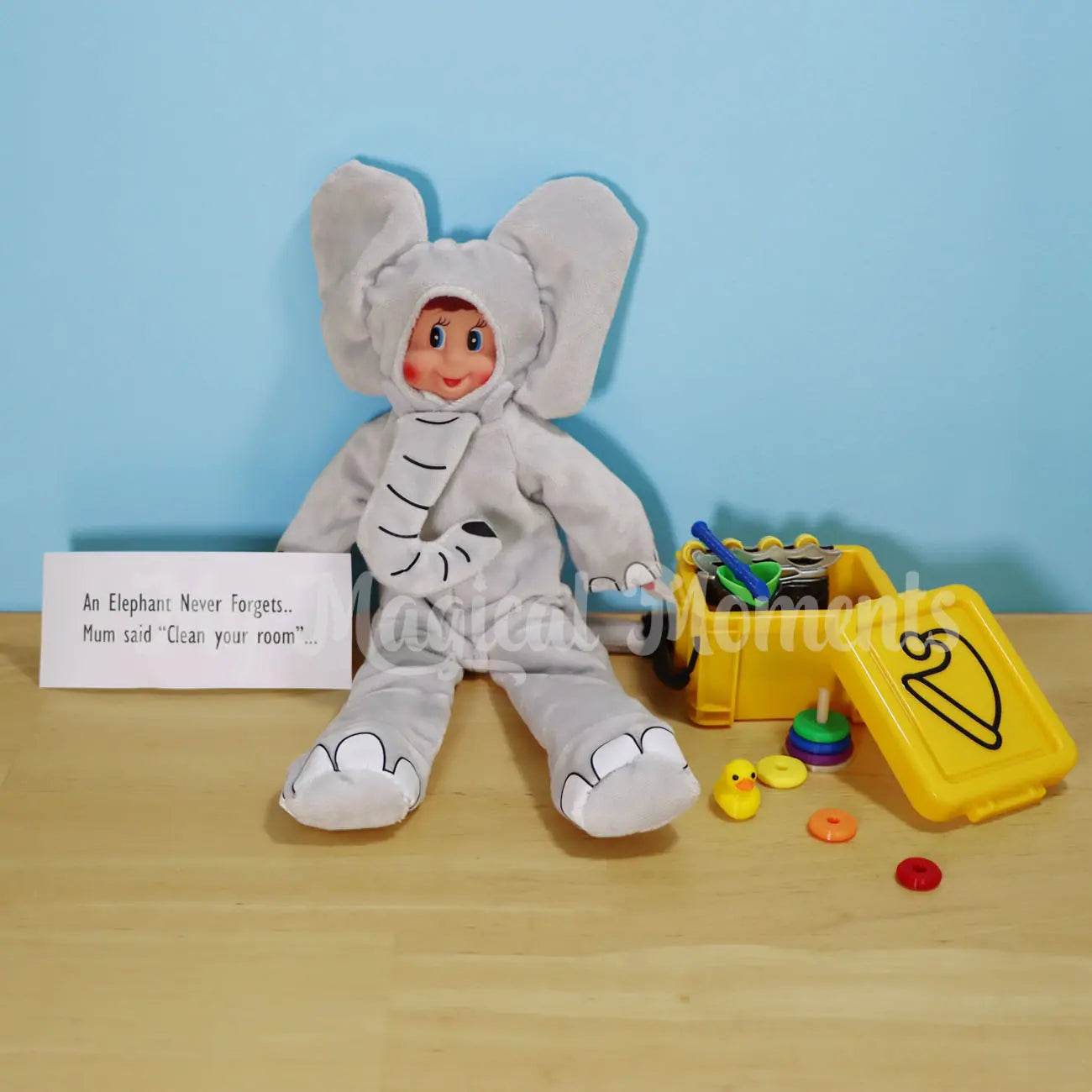 elf wearing an elephant costume with an elf sized storage container with mini elf accessories, rubber ducky, ring stacker, roller blades and recorder
