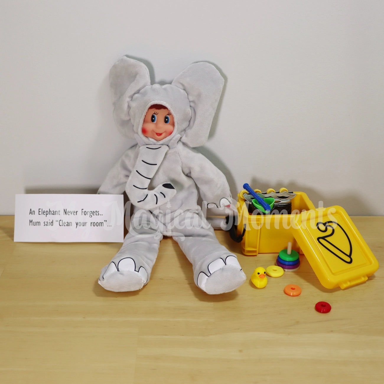 elf wearing an elephant costume with an elf sized storage container with mini elf accessories, rubber ducky, ring stacker, roller blades and recorder