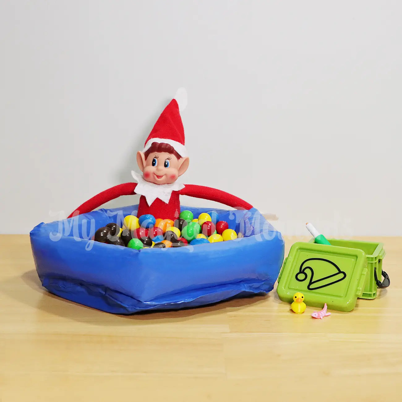 Elves behavin badly playing in an inflatable ball pit with m&ms and a small container with an axolotl fidget, a rubber duck and a water gun