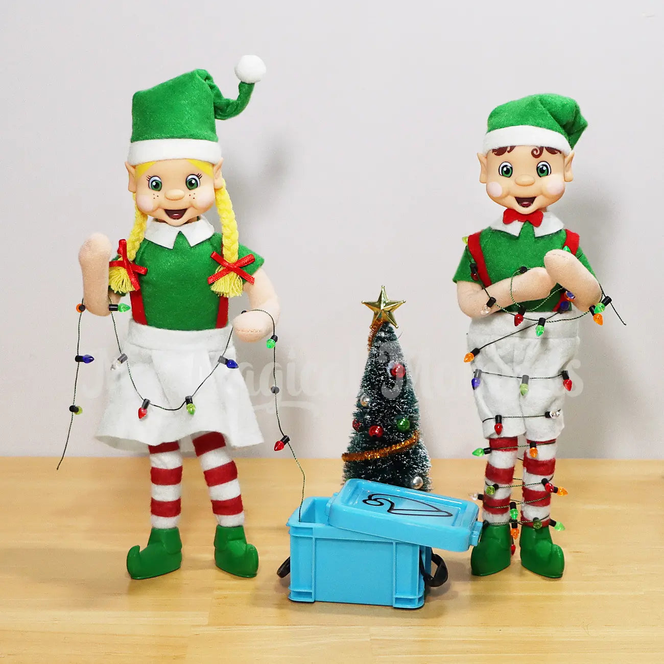 My Elf Friends Standing and holding mini Christmas Lights, Brown Hair boy is tangled in the lights coming out of an elf sized container and a Christmas tree