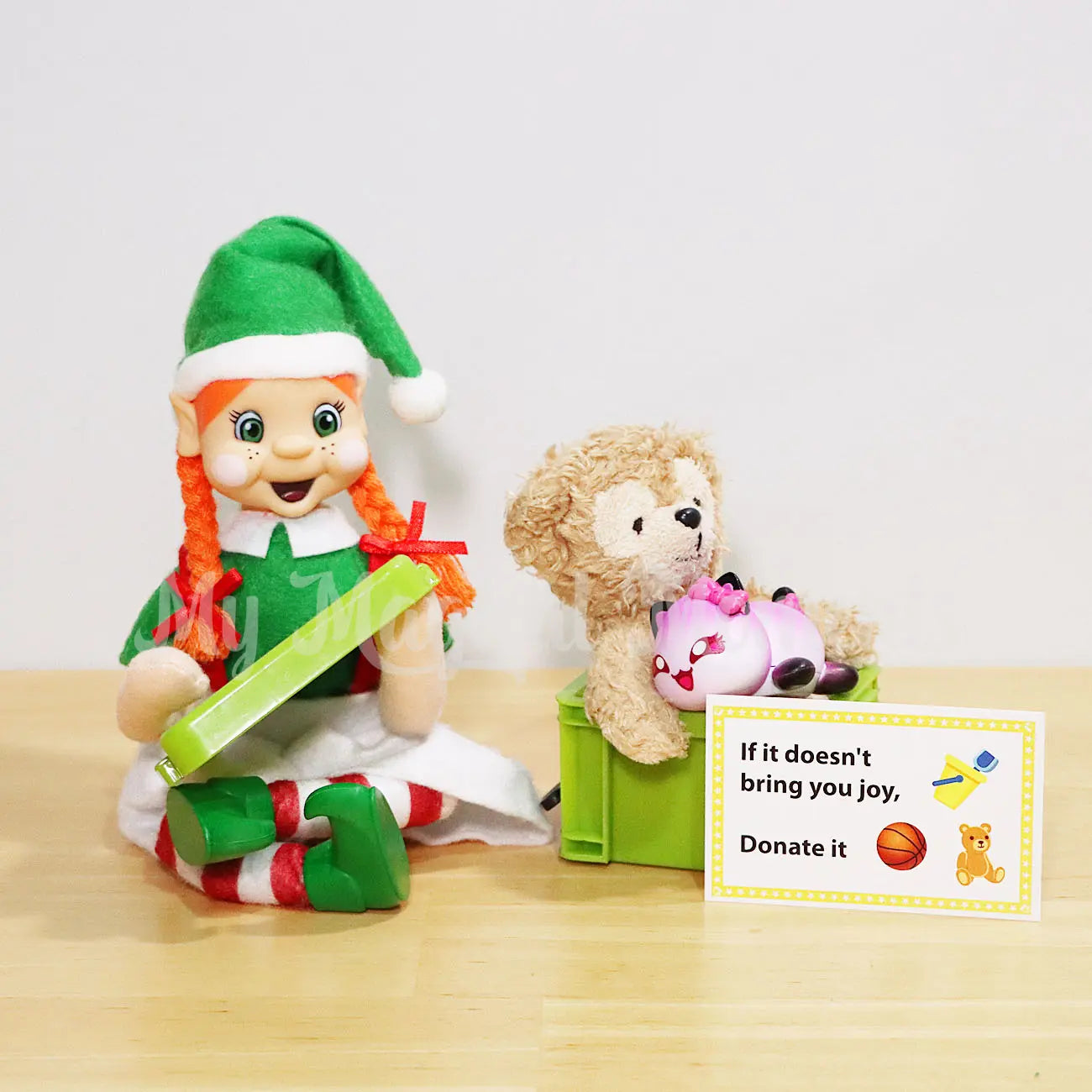 Orange hair bendable My Friends Elf holding a storage container lid with a box full of old toys to donate