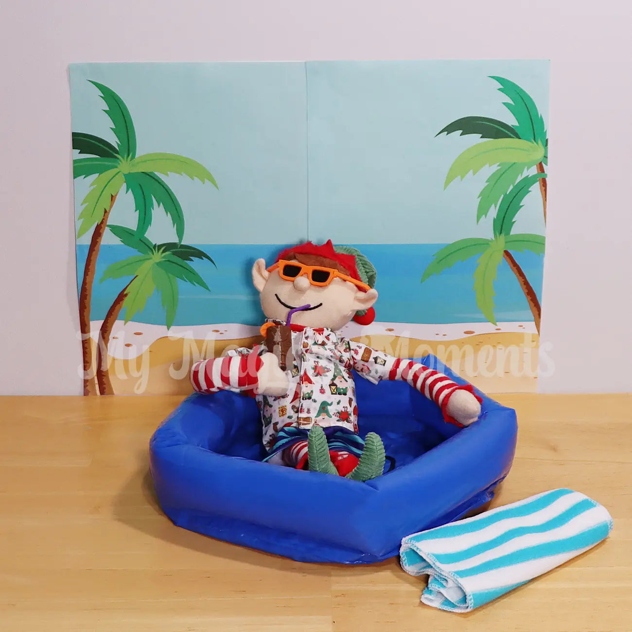 An Elf For Christmas wearing an Hawaiian shirt drinking a tiki cup with a beach background and towel