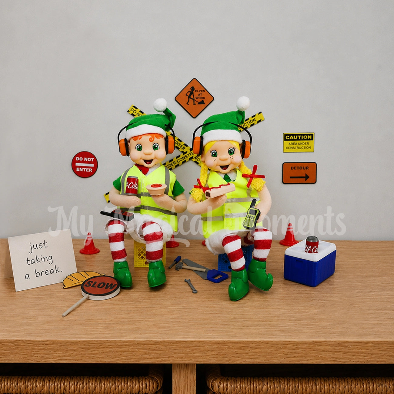 Elves dressed as tradies wearing headphones with pies & sausage rolls on a smoke-o at a construction site