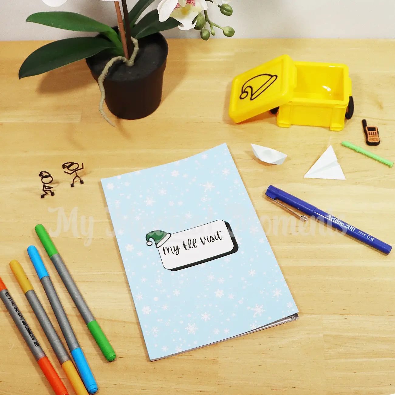 Elf Visit Planner sitting on a desk with elf props and pens