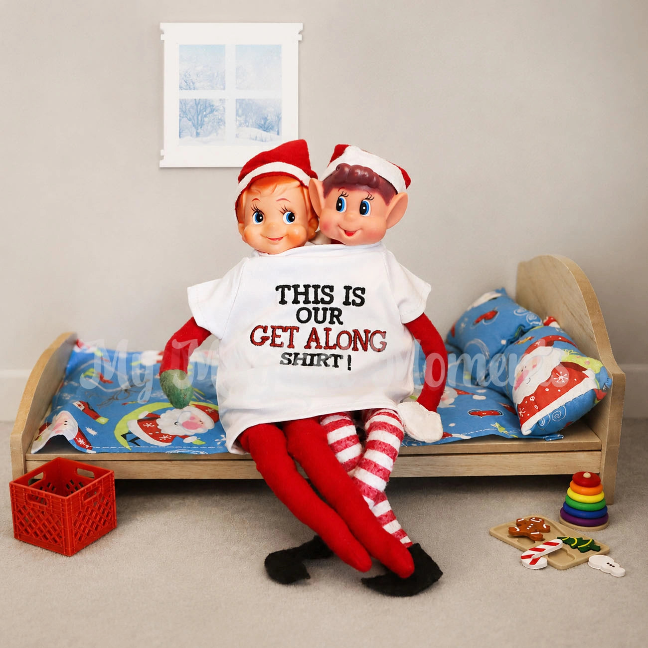 Elves wearing a get along shirt on a mini wooden bed with elf props