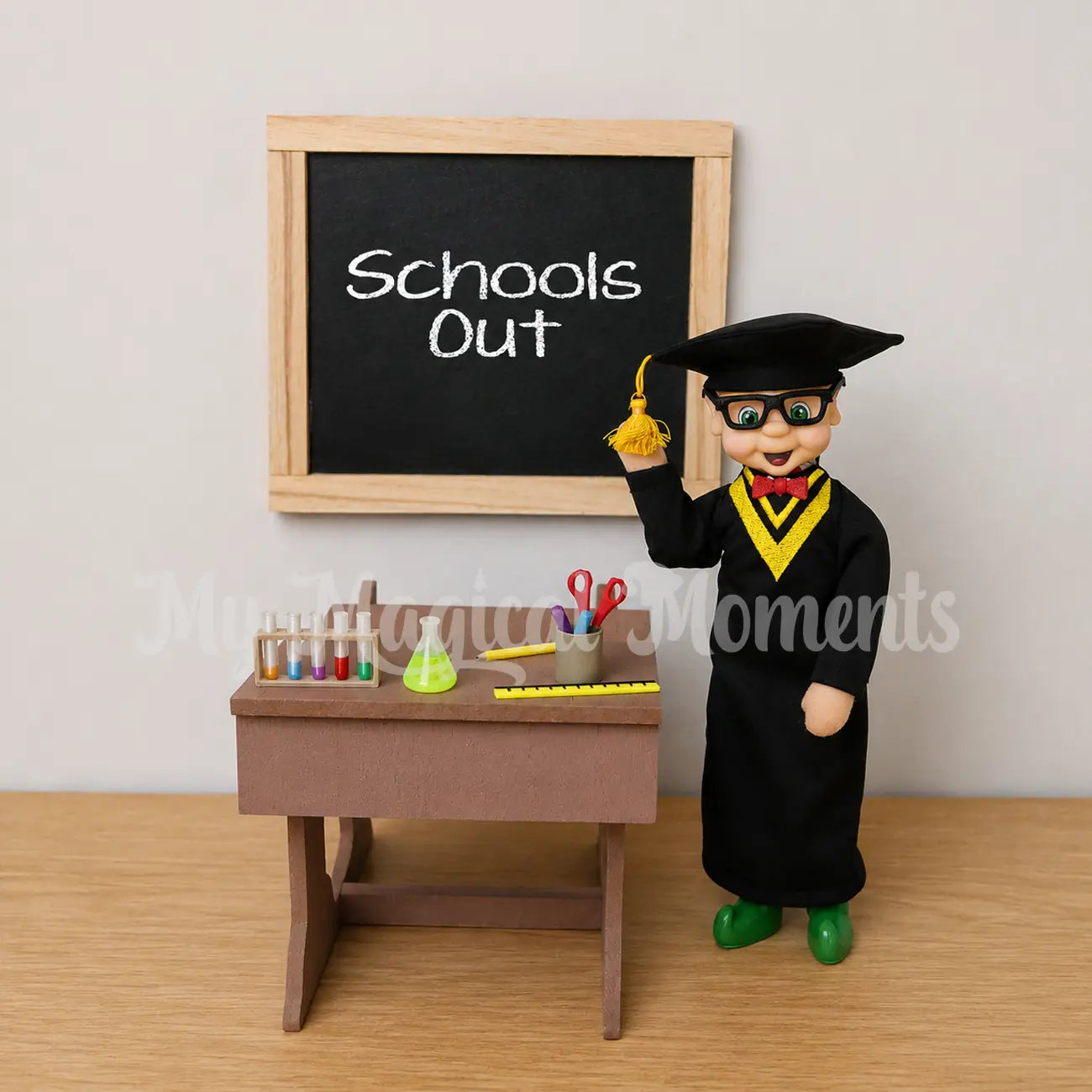 Elf wearing a graduation outfit in front of school desk and mini school supplies