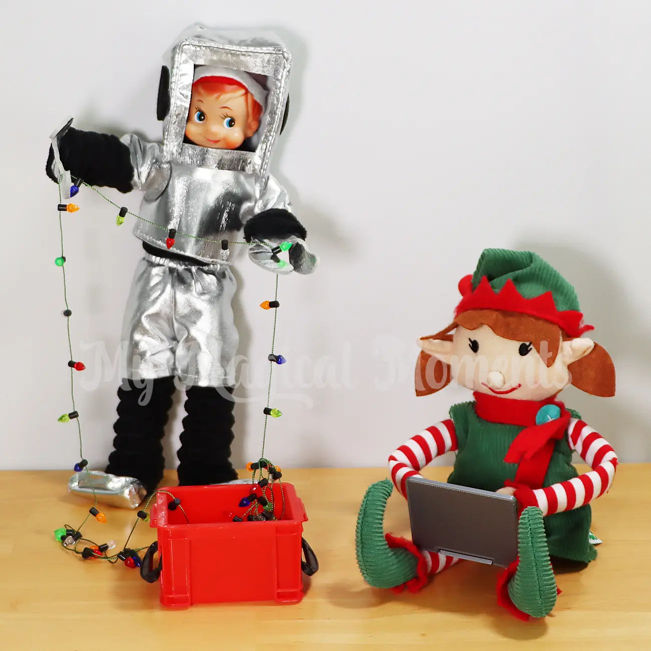 elf wearing a robot costume setting up Christmas lights from a container with an elf for Christmas elf using a mini laptop