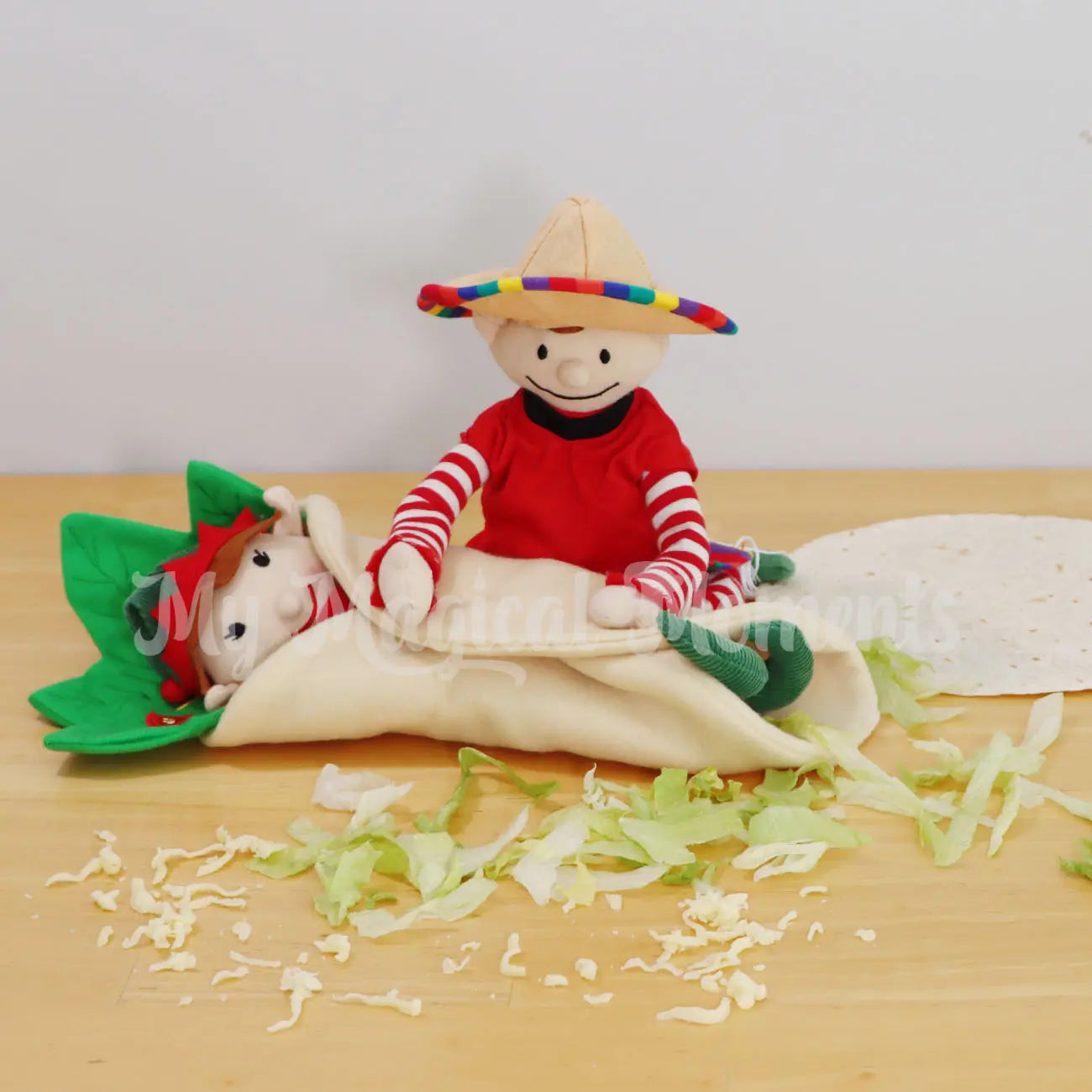 Elf wearing a Mexican festive outfit and sombrero rolling an elf into a burrito