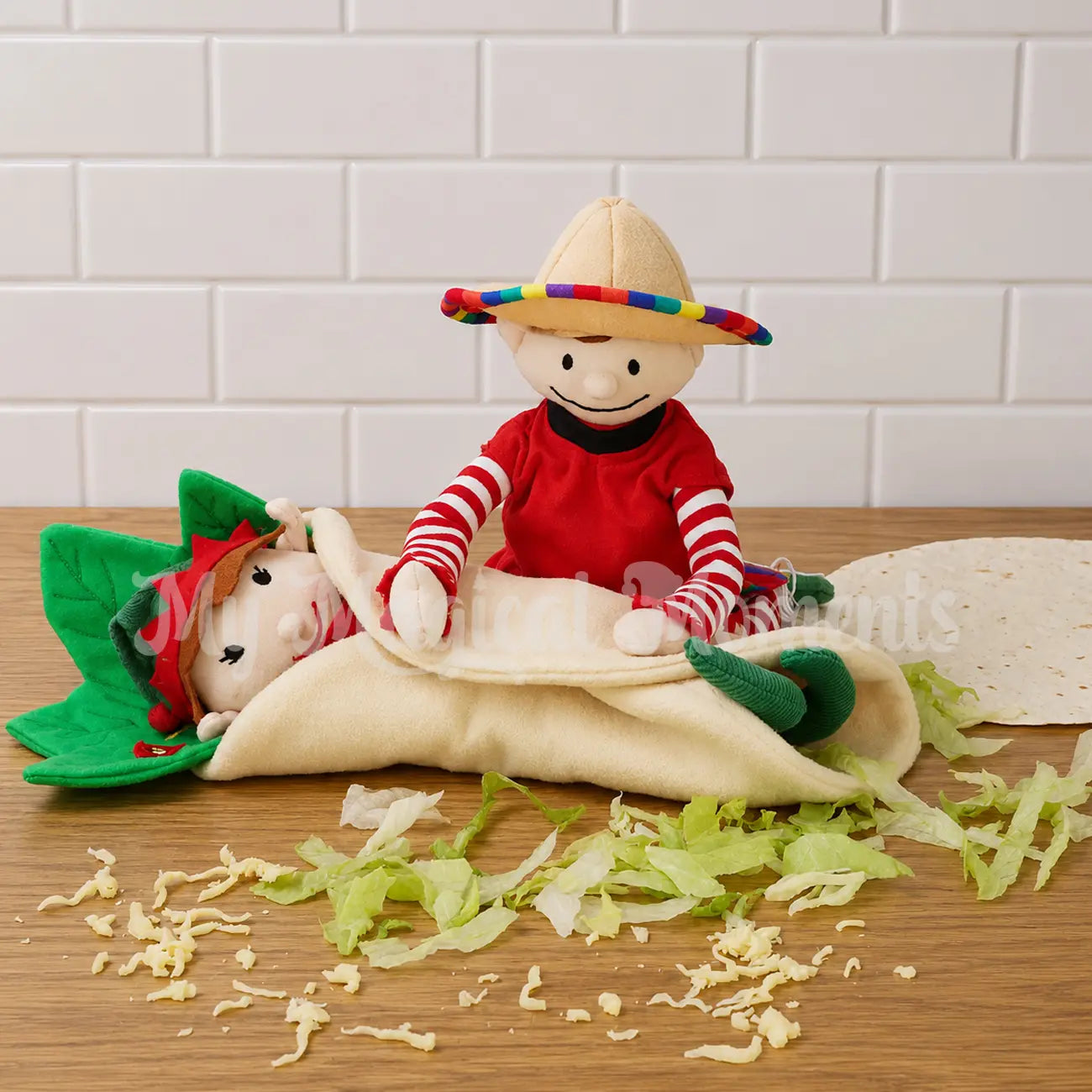 Elf wearing a Mexican festive outfit and sombrero rolling an elf into a burrito