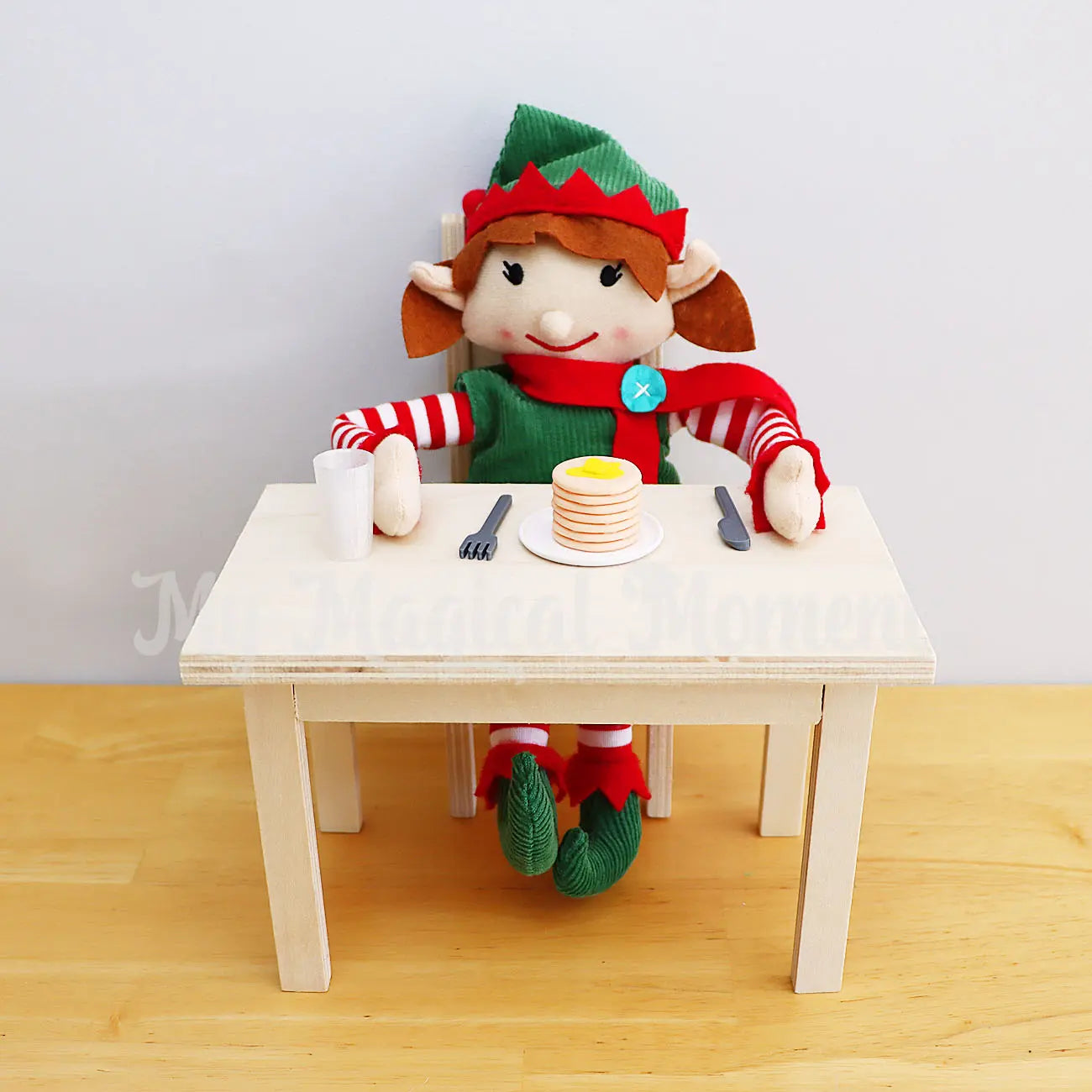 Elf eating a pancake stack with elf sized utensils on a mini wooden table