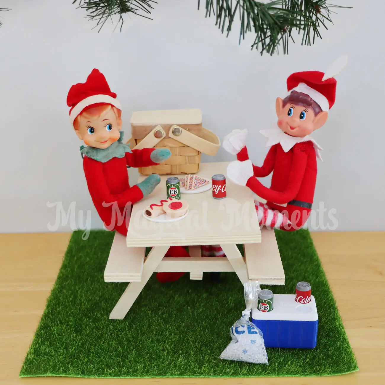 Elf having a picnic under the Christmas tree, with picnic basket and mini cola and beer