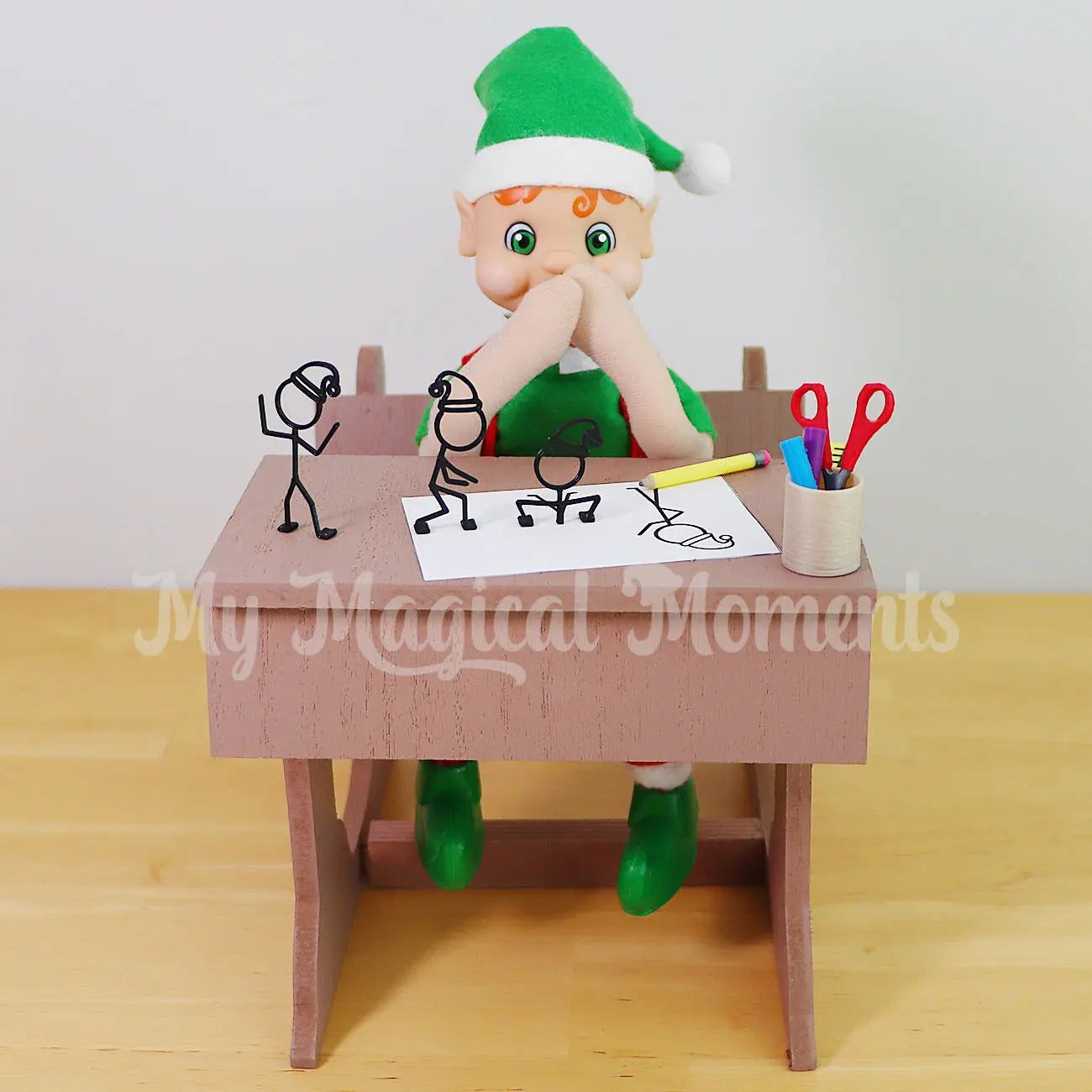 My Elf Friends Orange Hair Bendable Elf sitting in a mini wooden school desk with 3d stick figures coming out of the page with mini pencils and scissors
