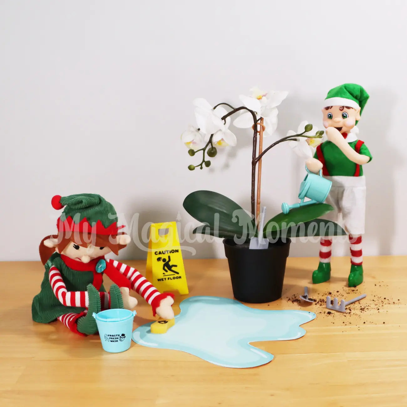 Elf For Christmas cleaning a spill with a bucket and mini sponge made by a brown hair boy My Elf Friends standing watering a plant. There is gardening tools and a caution wet floor sign