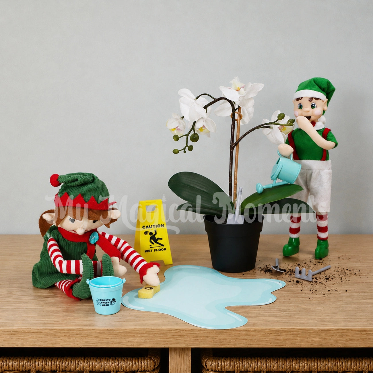 Elf For Christmas cleaning a spill with a bucket and mini sponge made by a brown hair boy My Elf Friends standing watering a plant. There is gardening tools and a caution wet floor sign