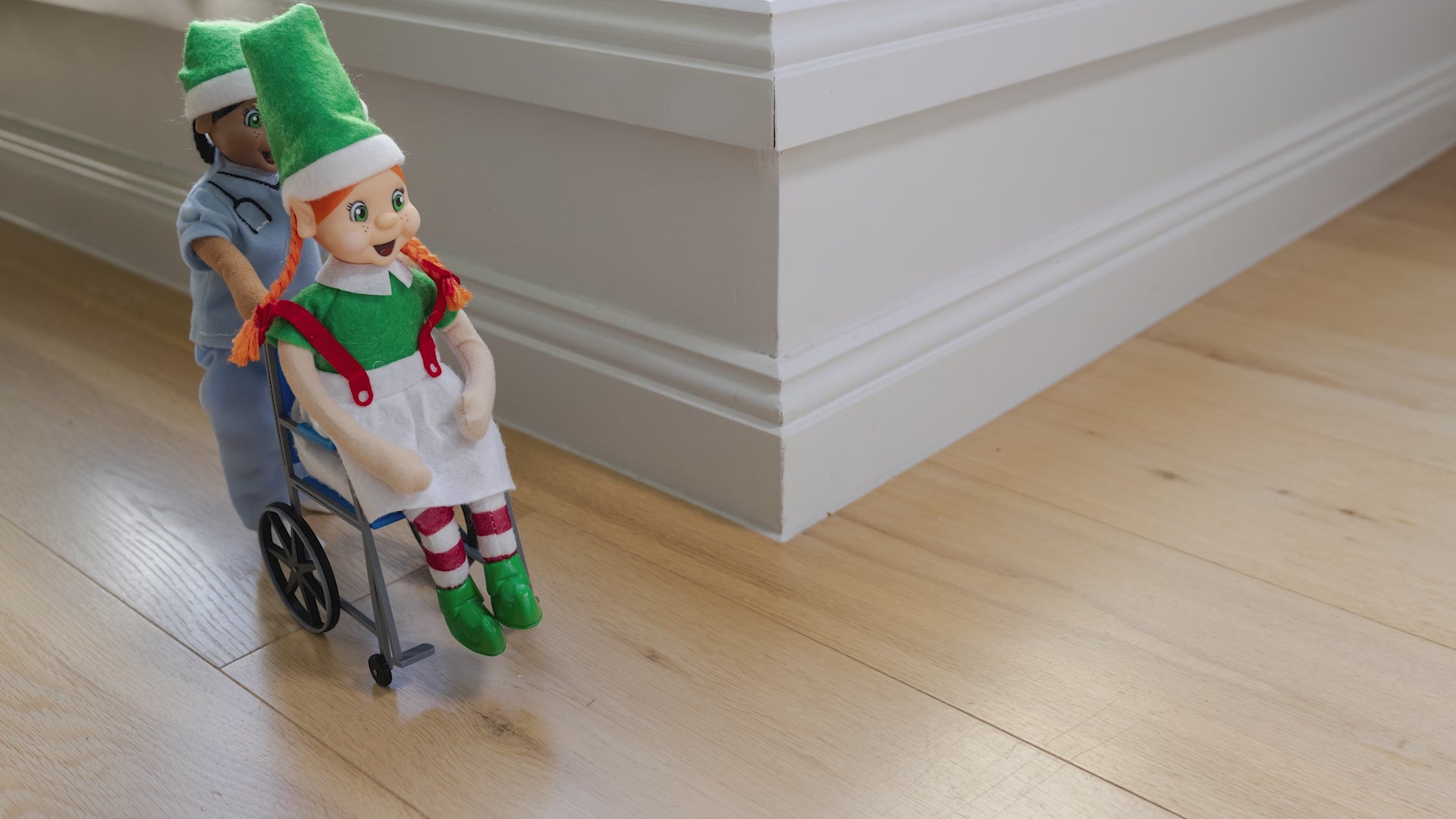 elf dressed as a nurse pushing an elf in a wheelchair
