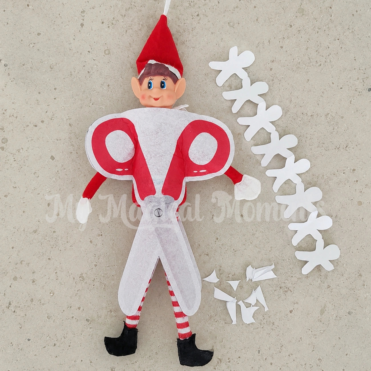 Elves behavin badly dressed in a pair of scissors with paper people cut out next to him