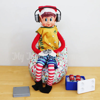 Elf wearing headphones playing a mini gaming set wearing an aussie singlet on a bean bag. With a mini esky filled with cola