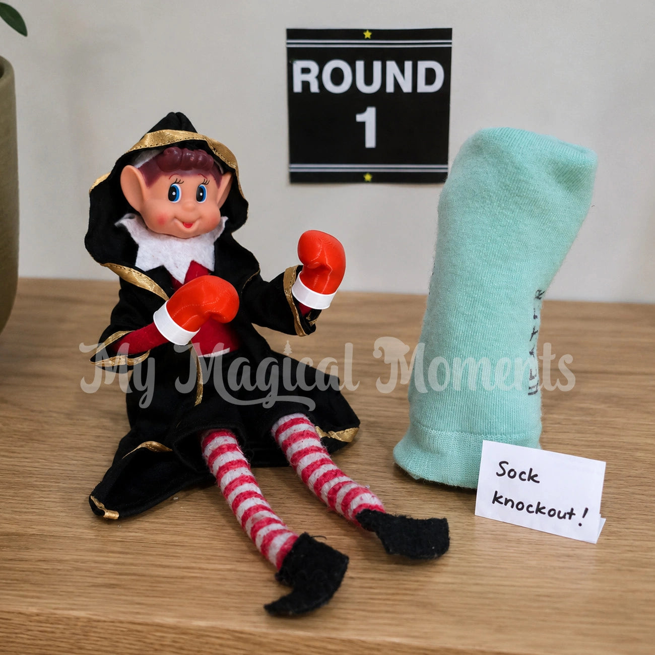 Elf wearing a boxing robe shorts and boxing gloves, having a match with a sock, with a note saying sock knockout. There's a round 1 printable on the wall