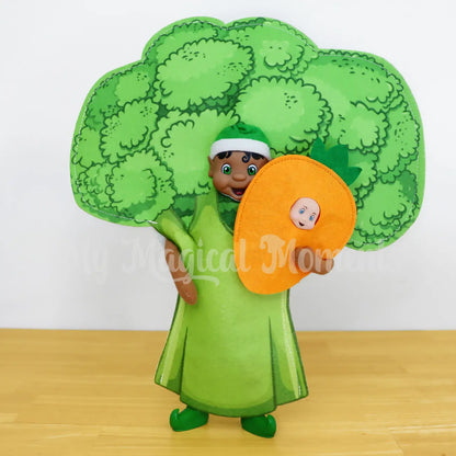 Elf wearing a broccoli costume holding an elf baby wearing a carrot costume