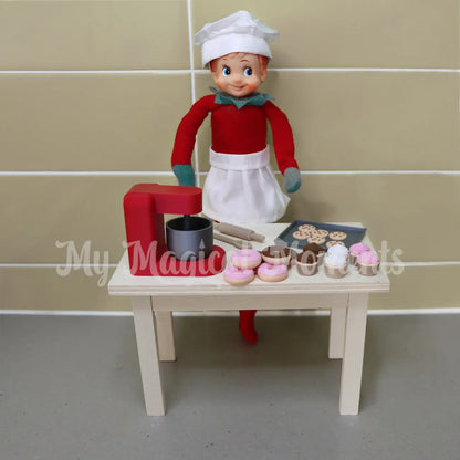 elf dressed as a chef baking in the kitchen with mini donuts, cupcakes and cookies