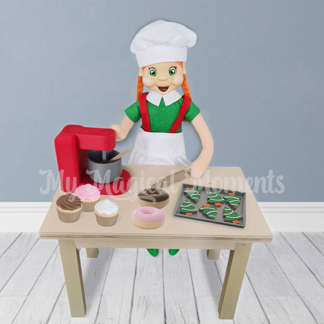 elf dressed as a chef using a red miniature baking mixer to make donuts, cupcakes a tiny gingerbread cookies