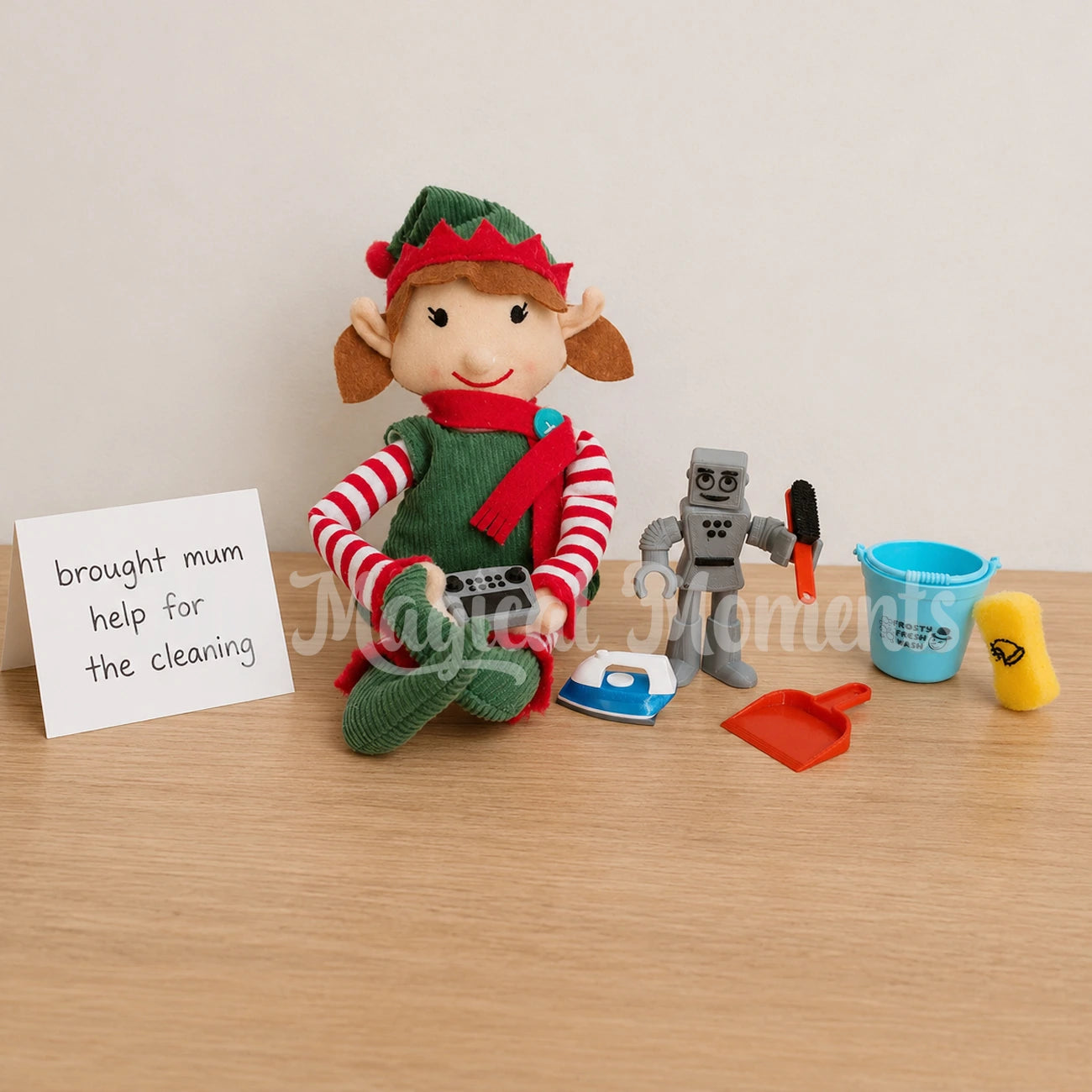 elf holding a remote control for a robot, the robot is holding a mini dust pan brush, with an miniature iron, bucket and sponge. There is a hand written note saying brought mum help for cleaning