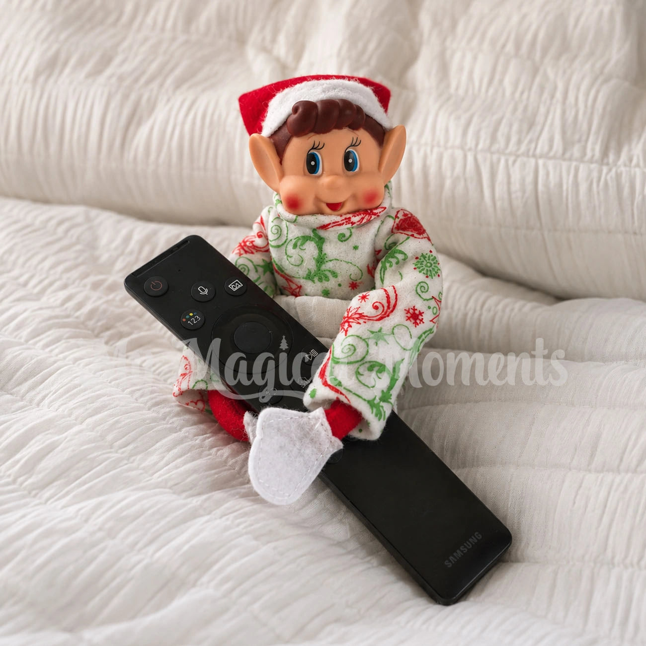 Elf wearing Christmas Ornament Pyjamas in bed with a remote