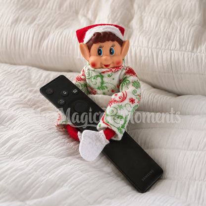 Elf wearing Christmas Ornament Pyjamas in bed with a remote