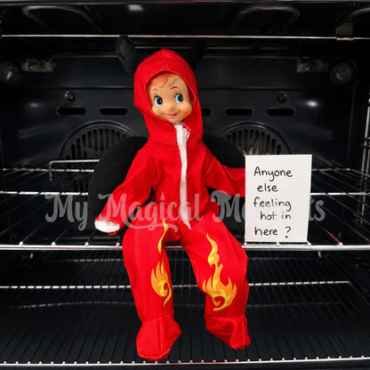 Elf wearing a devil costume, sitting in the oven, with a note saying anyone else feeling hot in here?