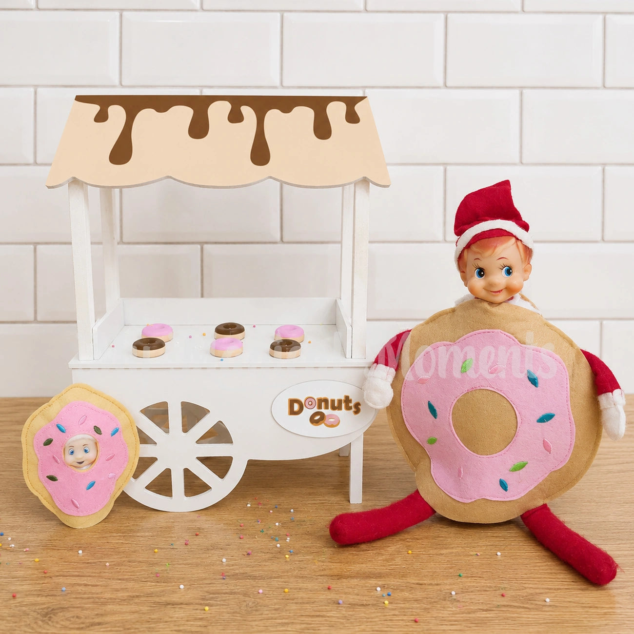 Elf wearing a donut costume in front of a mini cart selling donuts with a baby elf dressed as a donut