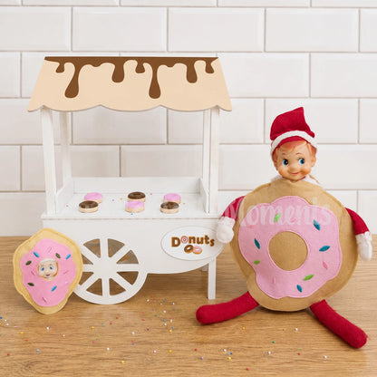 Elf wearing a donut costume in front of a mini cart selling donuts with a baby elf dressed as a donut