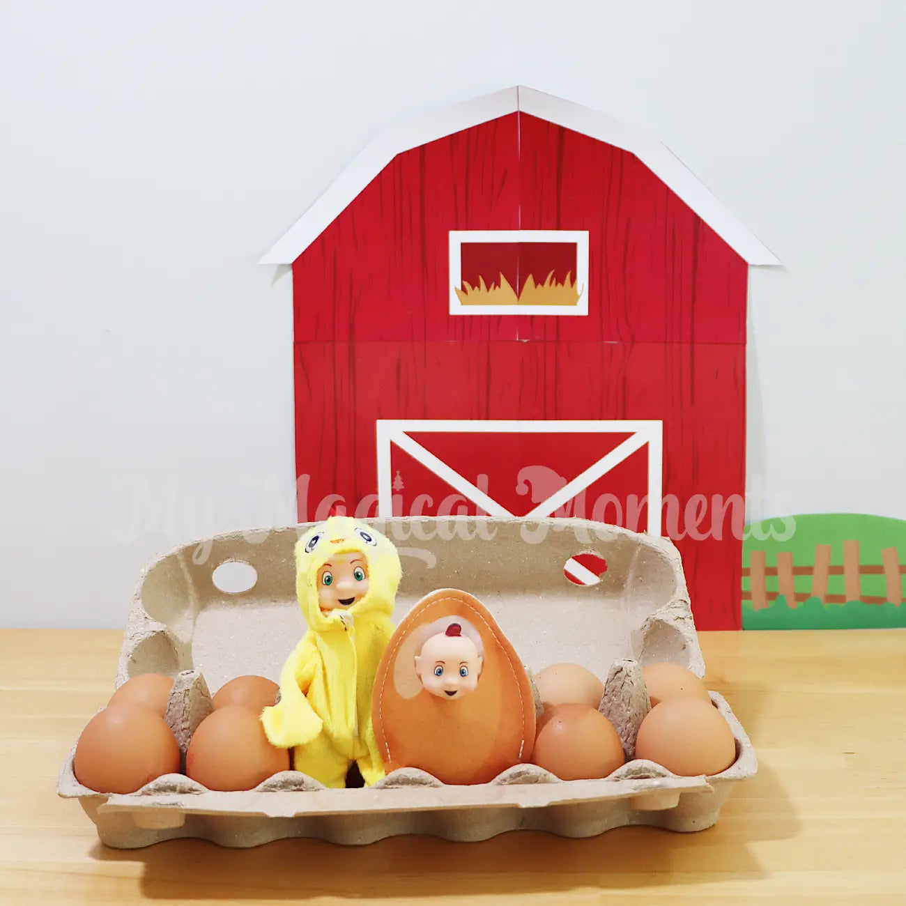 Toddler Elf wearing a chick costume with an elf baby wearing an egg costume in an egg carton in front of elf barn printable 