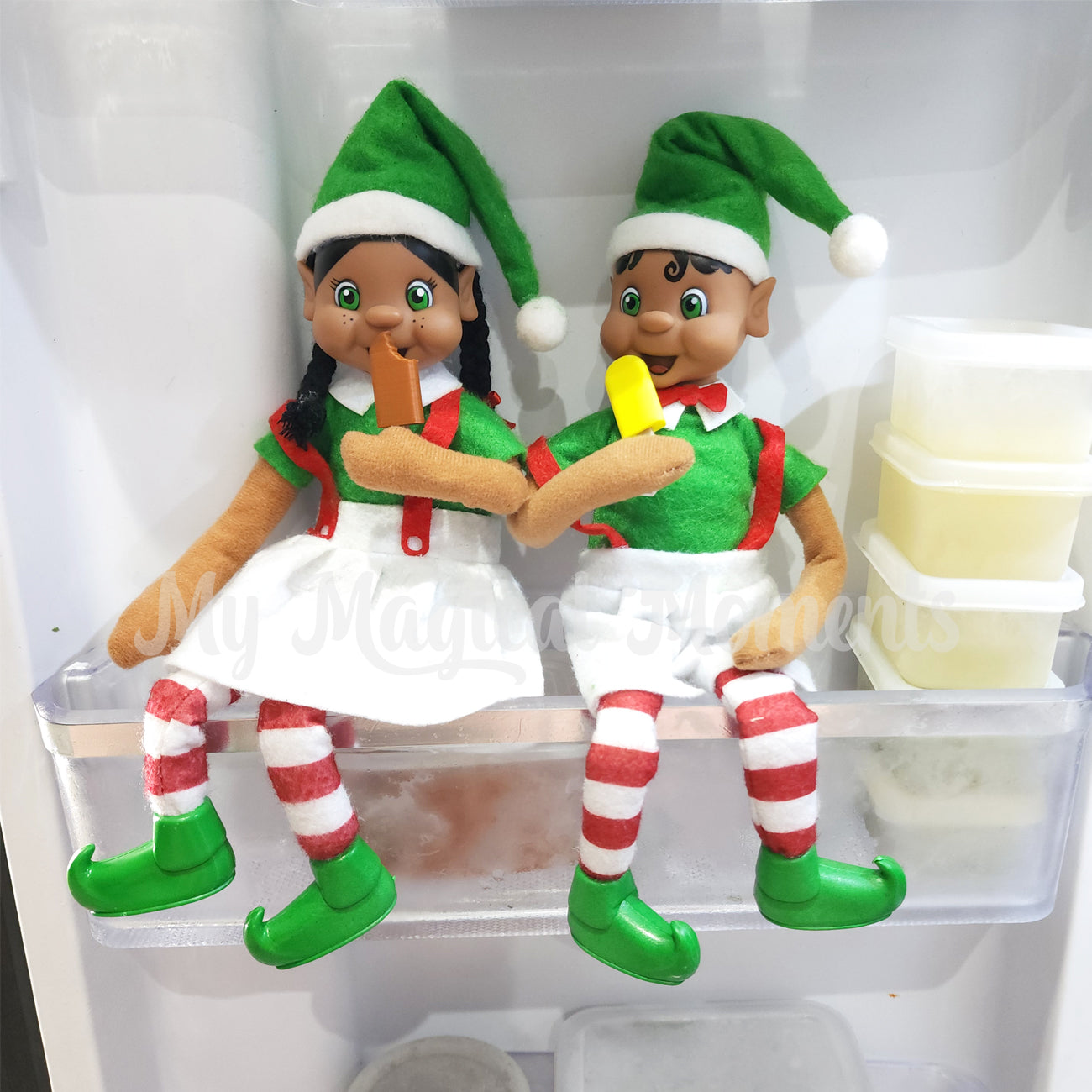 Two elves sitting in a freezer eating mini paddle pop ice creams