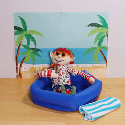 An Elf For Christmas wearing an Hawaiian shirt drinking a tiki cup with a beach background and towel