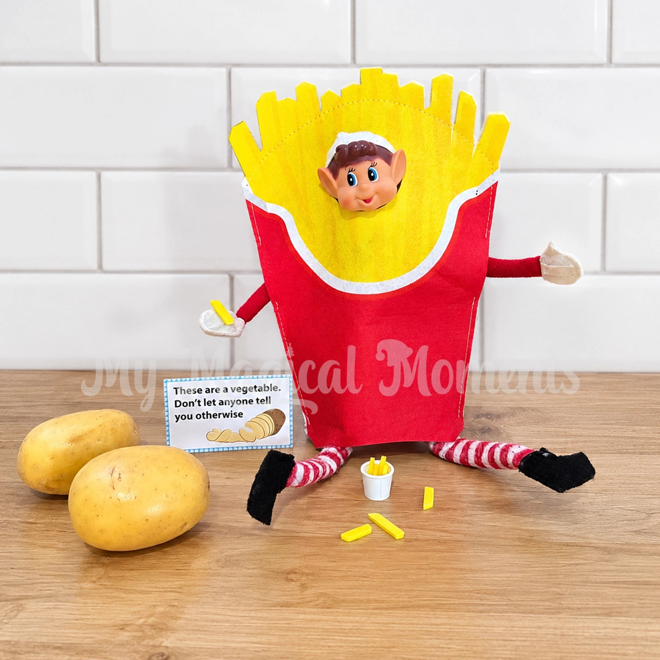 Elf wearing a french fries costume, with mini elf prop chips, potatoes and a sign saying these are a vegetable, don't let anyone tell you otherwise
