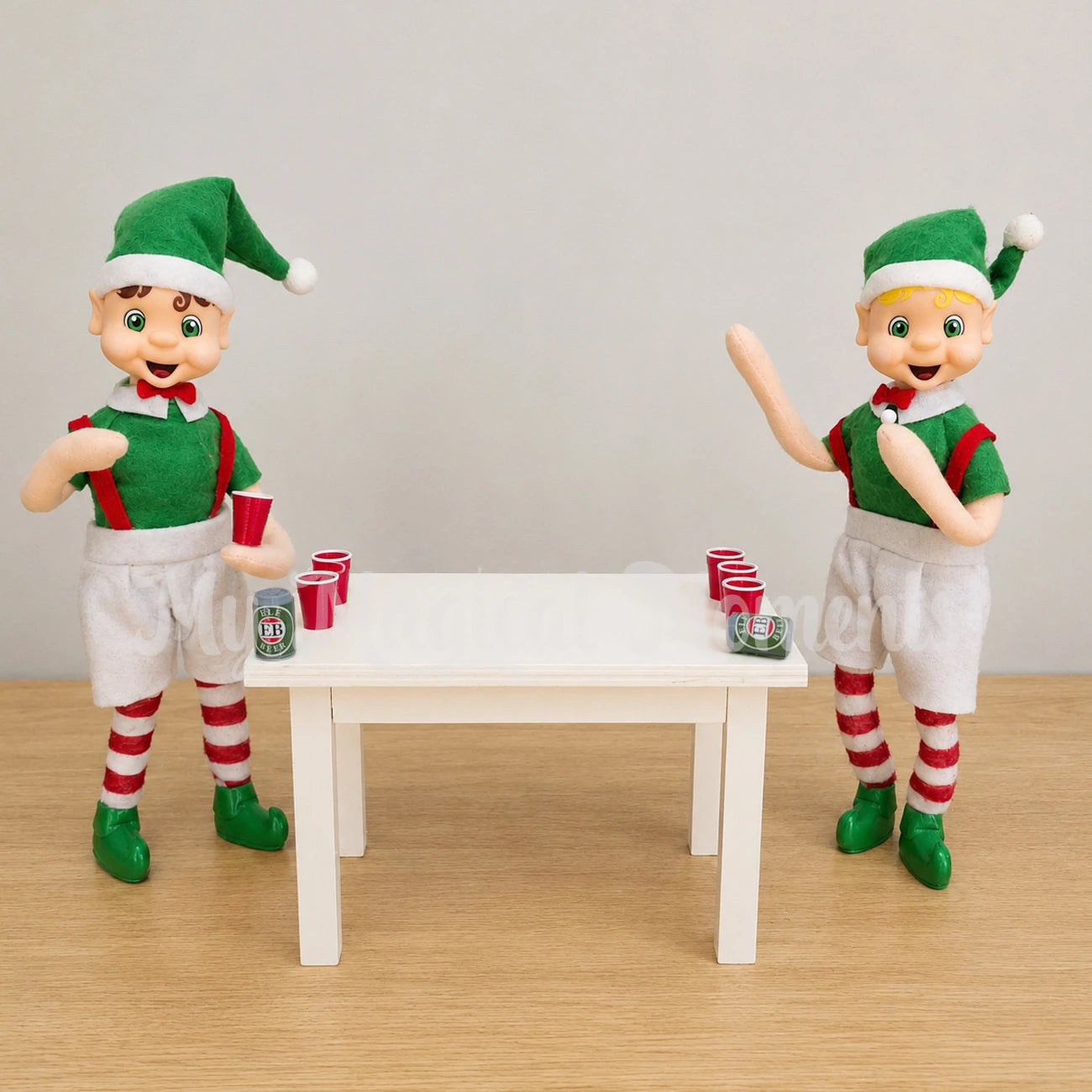 Brown hair bendable standing elf playing beer pong with a blonde hair bendable elf. They have mini beers on a wooden table and red cups