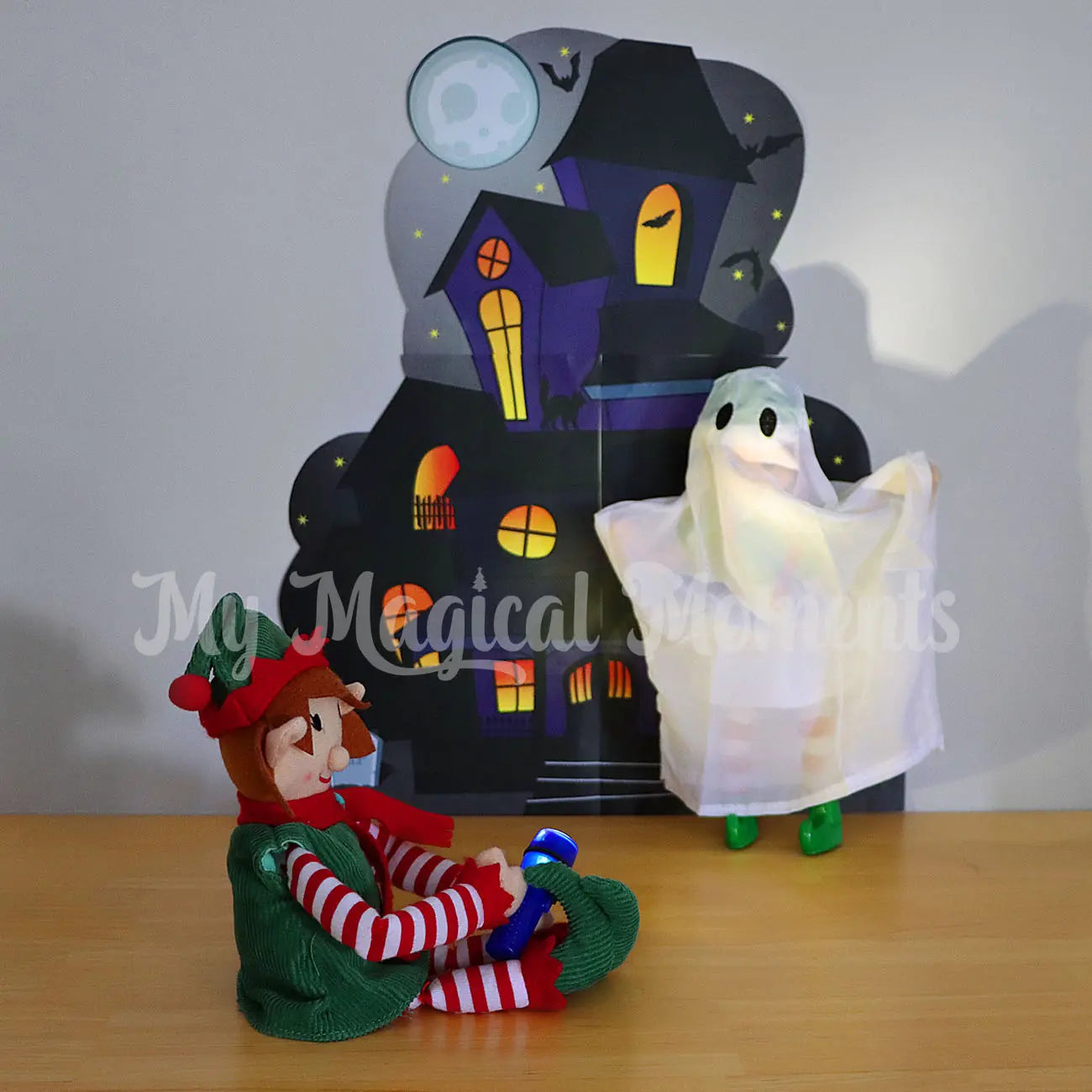 Elf finding an elf dressed as a ghost in front of a haunted mansion printable with a mini torch