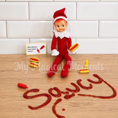Elf holding, mini hot dog props with mini tomato sauce, mustard and the words Saucy spelt out with ketchup