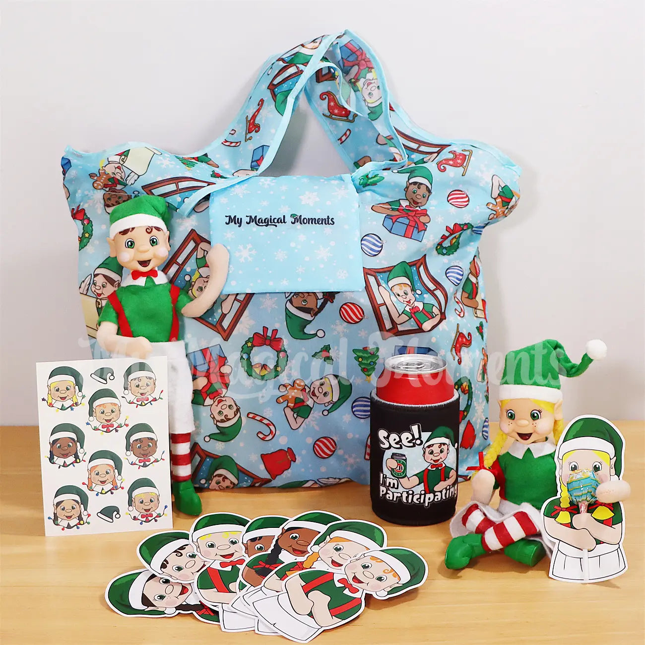 My Magical Moments Merch, Elf Friends Shopping Bag, Stubby Cooler, Lollipop Holders and Temporary Tattoos With My Elf Friends featured on them. Brown hair boy Elf standing with blonde hair girl sitting