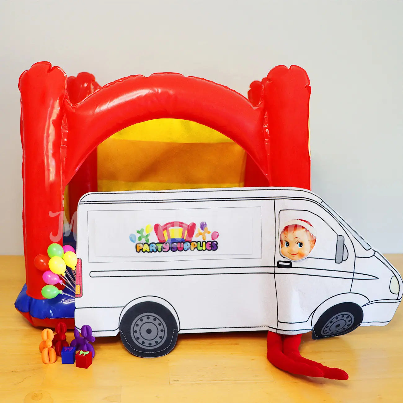 Elf wearing a party supply Van in front of a jumping castle with balloons and balloon dogs setting up for a party