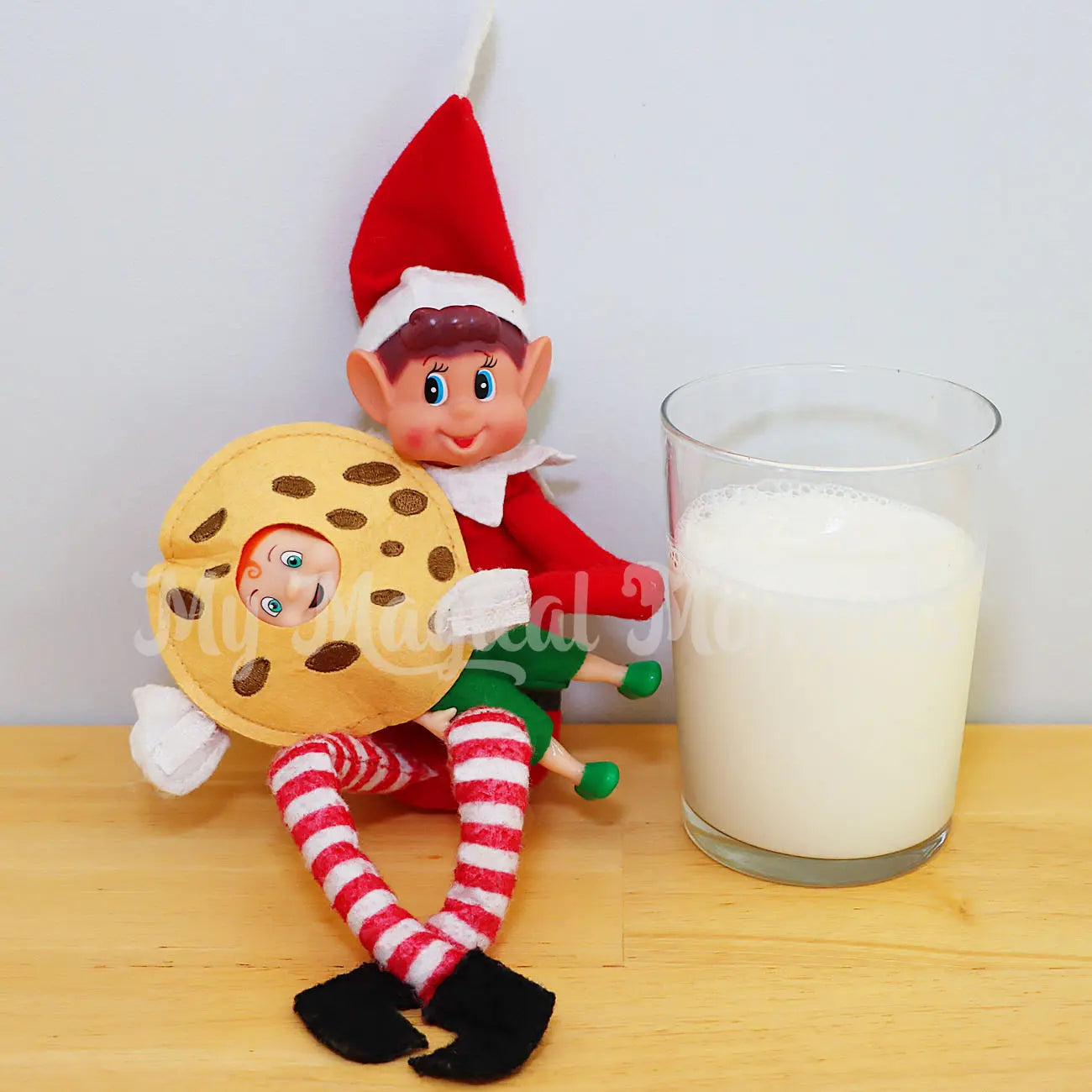 Elf holding an elf baby with a cookie with a glass of milk